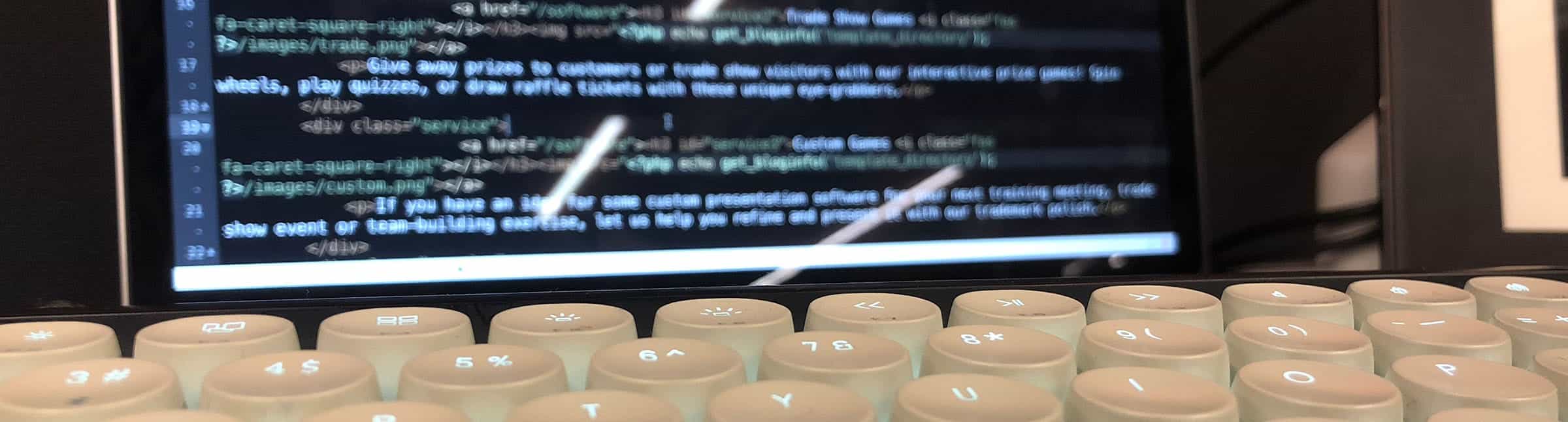 Image: A mechanical keyboard, with HTML code blurred in the background.
